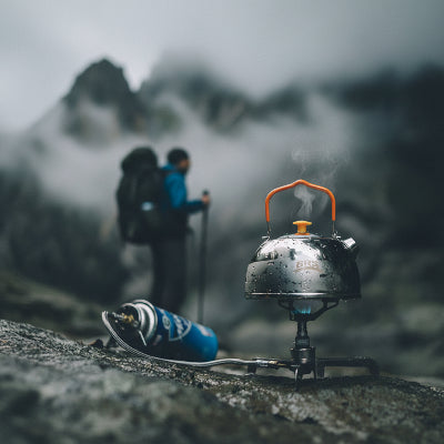 Mini réchaud à gaz avec bouilloire et randonneur admirant le panorama 